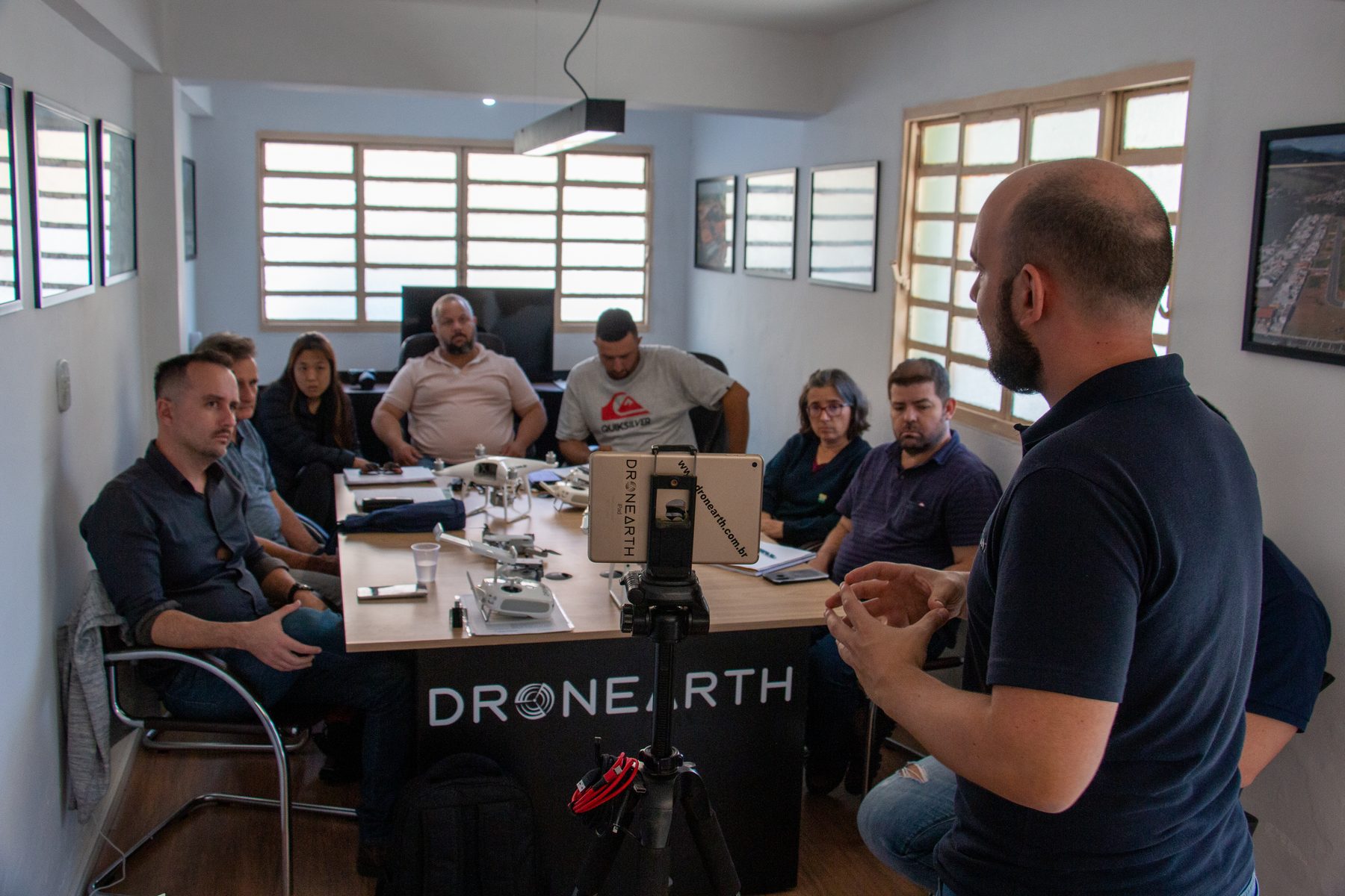 Turma em aula teórica na escola de drones da Dronearth, com drones sobre a mesa e instrutor à frente