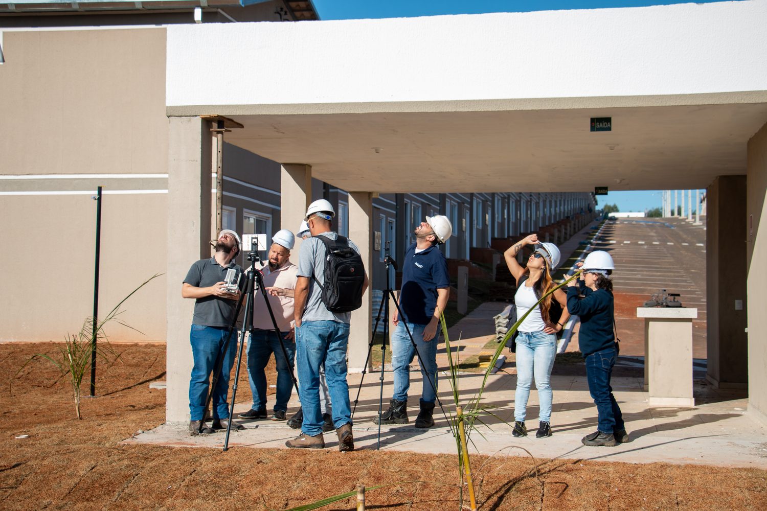 Equipe de capacete acompanha o voo de um drone durante aula prática em canteiro de obras
